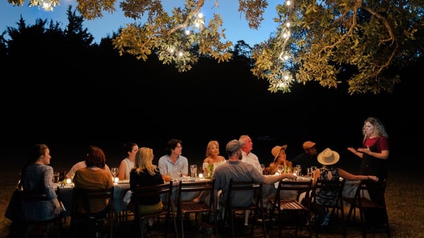 Group dining at long table outdoors at dusk