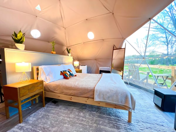 Queen bed inside a luxury glamping dome with skylights and window facing the garden