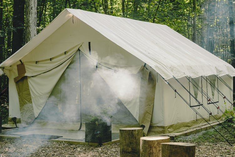 glamping tent with campfire and tree stump seating